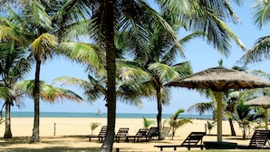 A beach with palm trees, lounge chairs, and a thatched umbrella. - Goldi Sands Hotel (Negombo)