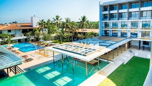 A rooftop pool area with a glass enclosure, palm trees, and a modern building with multiple balconies. - Goldi Sands Hotel (Negombo)
