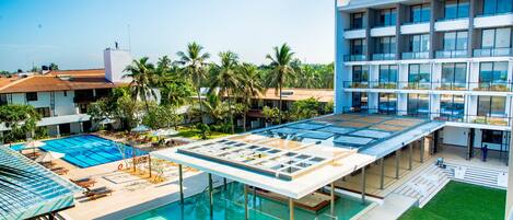 A rooftop pool area with a glass enclosure, palm trees, and a modern building with multiple balconies.