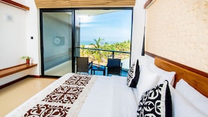 A hotel room with a balcony, a bed with patterned bedding, and a view of the ocean. - Goldi Sands Hotel (Negombo)