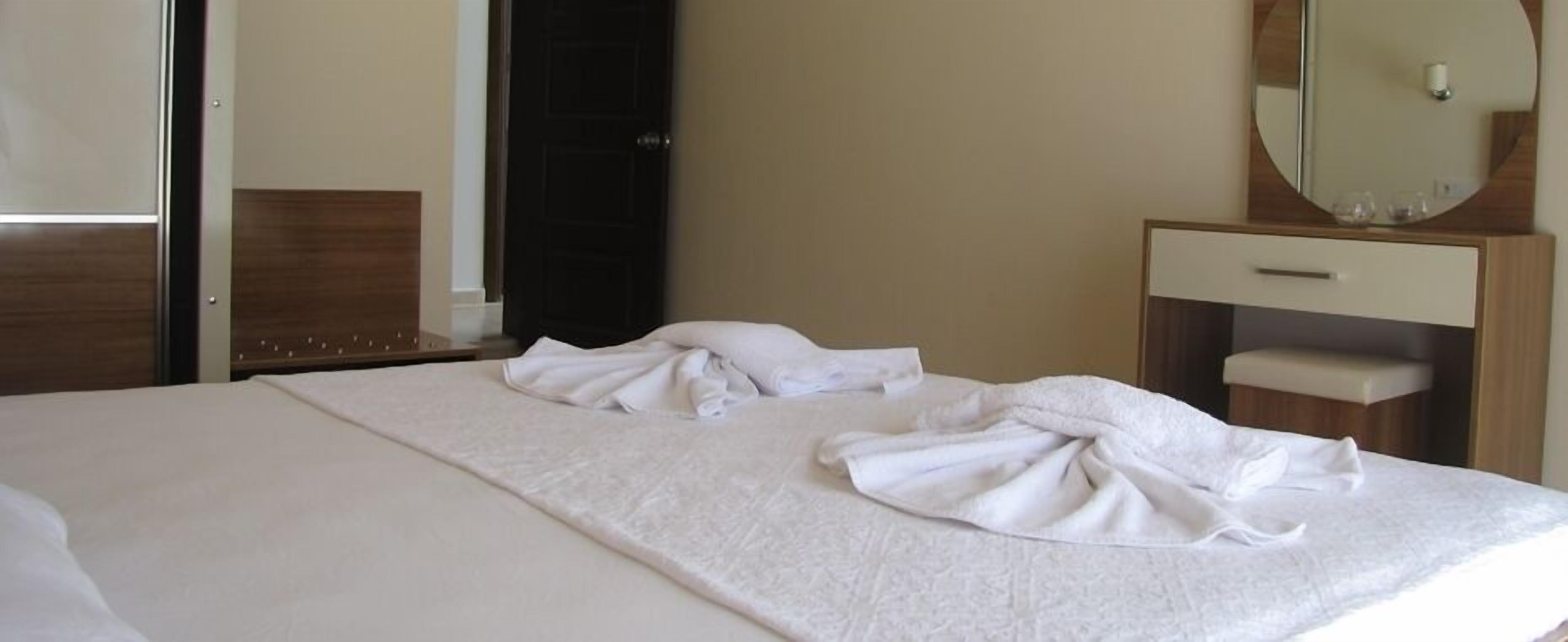 A hotel room with a bed, a wooden nightstand, a mirror, and a small wooden cabinet.