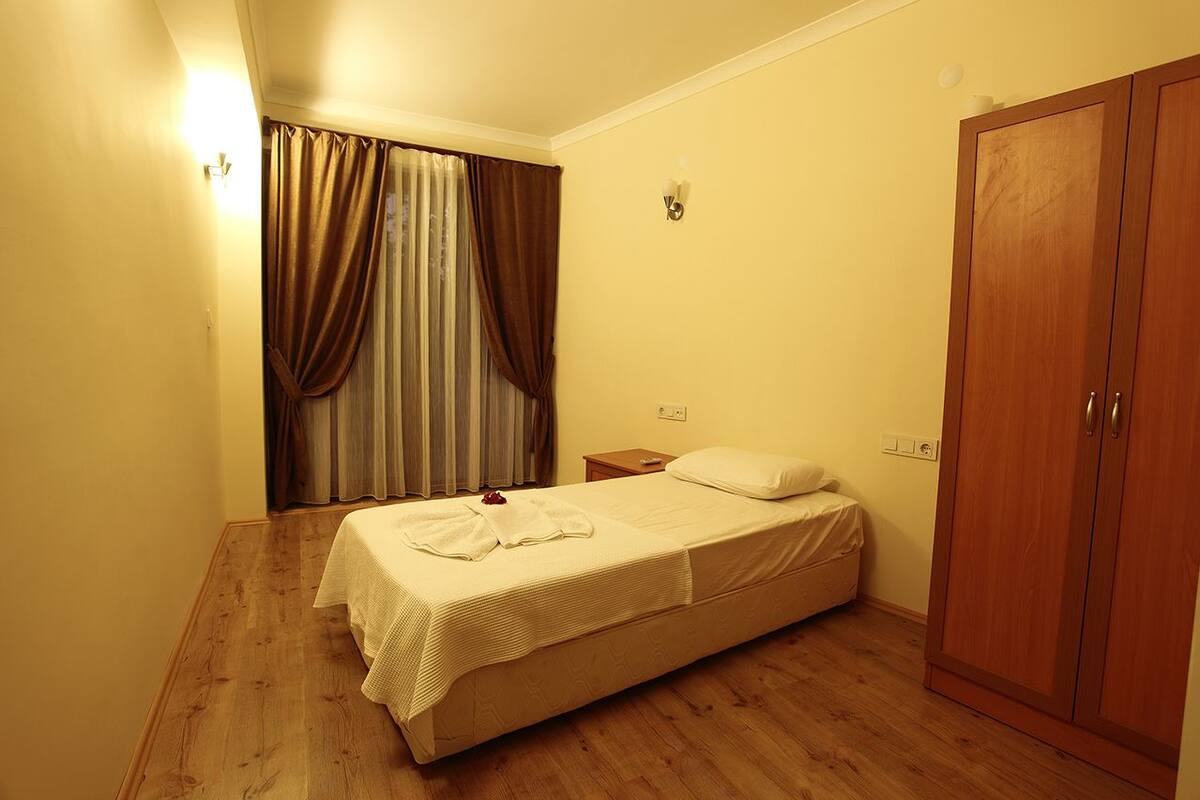 A small, neatly arranged bedroom with a single bed, a nightstand, a wardrobe, and a window with curtains.