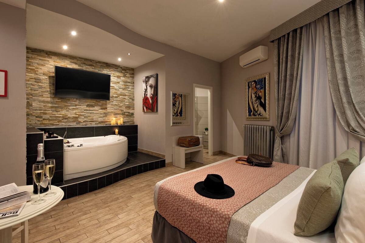 Un dormitorio moderno con una cama grande, un televisor montado en la pared, una bañera y obras de arte en las paredes.