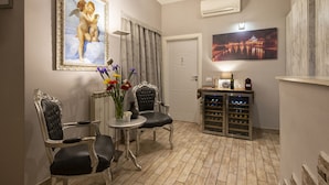A cozy room with two upholstered chairs, a small table with a vase of flowers, and a wine cooler. - Five Rooms Rome Guesthouse (Rome)