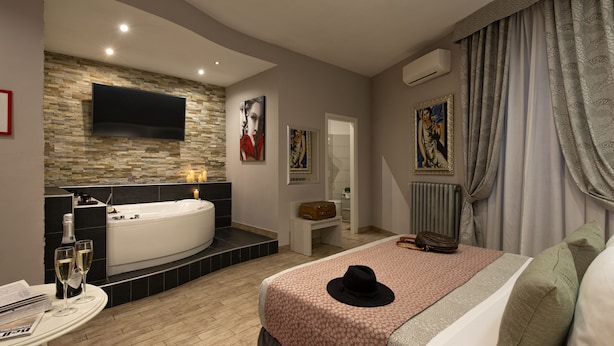 A modern bedroom with a large bed, a wall-mounted TV, a bathtub, and artwork on the walls. - Five Rooms Rome Guesthouse (Rome)