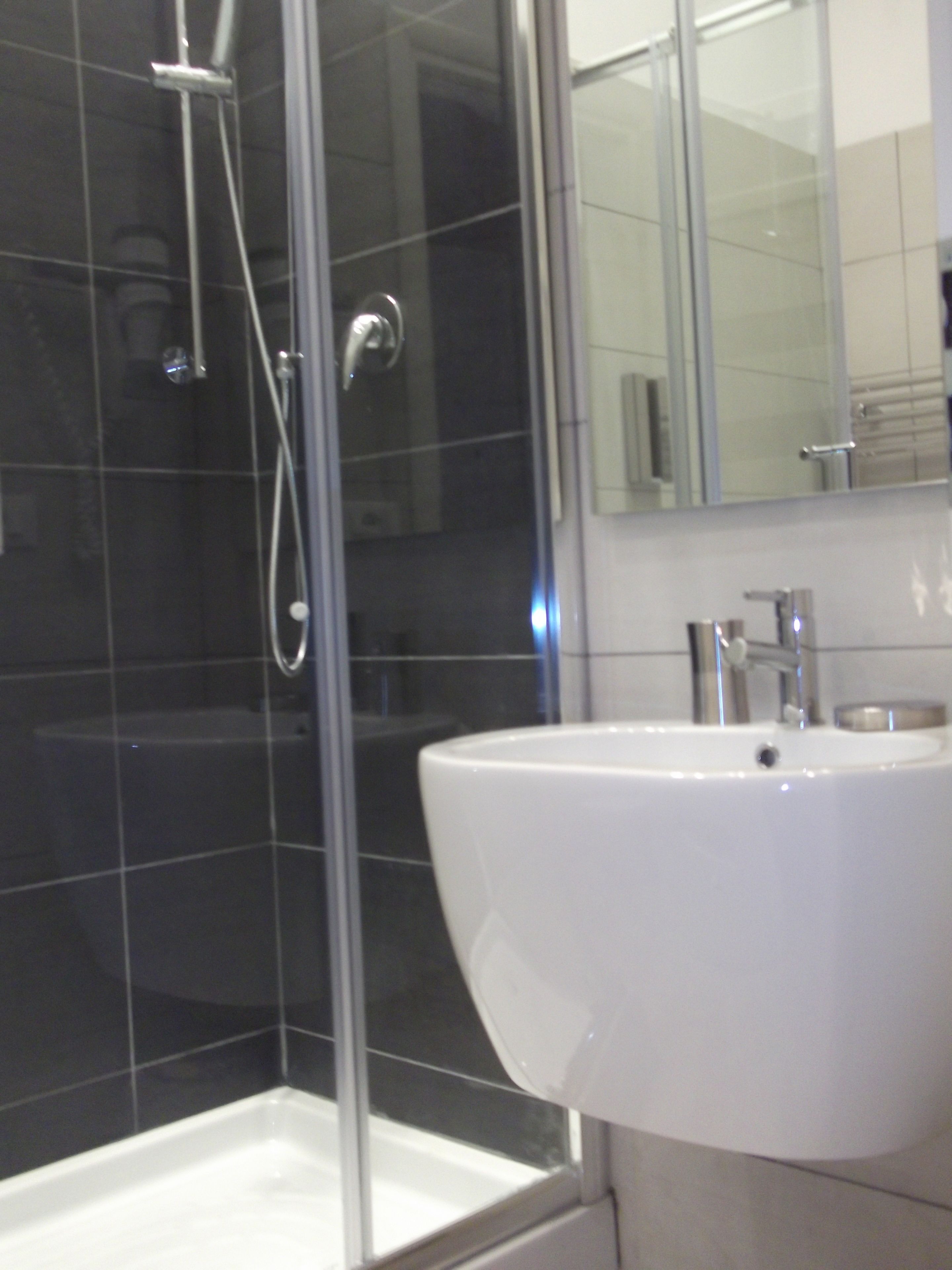 Ein Badezimmer mit einer gläsernen Duschkabine, einem weißen Waschbecken und einem Spiegel darüber.