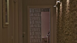 A hallway with a wooden floor, a stone wall on the right, and a door leading to a room with a patterned wallpaper. - Five Rooms Rome Guesthouse (Rome)