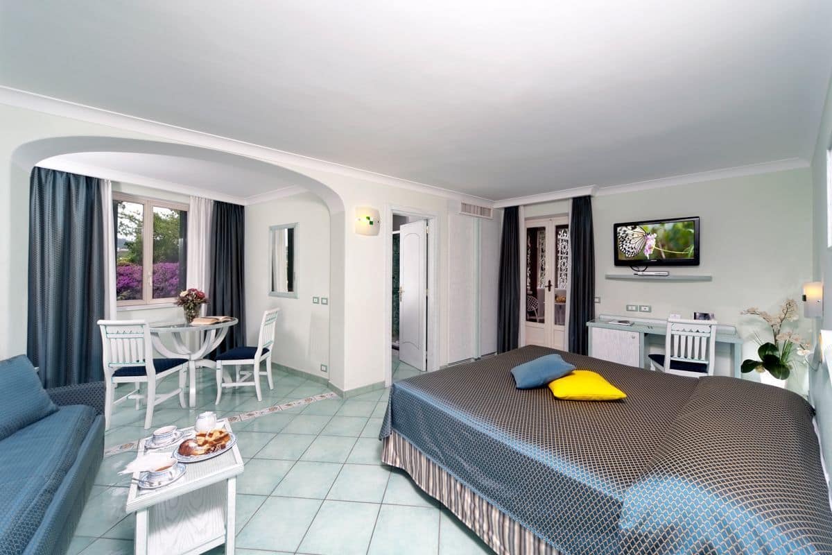 A hotel room with a bed, a desk, a chair, a TV, and a window with curtains.
