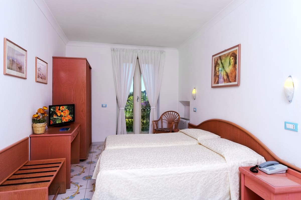 A hotel room with a bed, a desk with a computer, a chair, and a window with curtains.