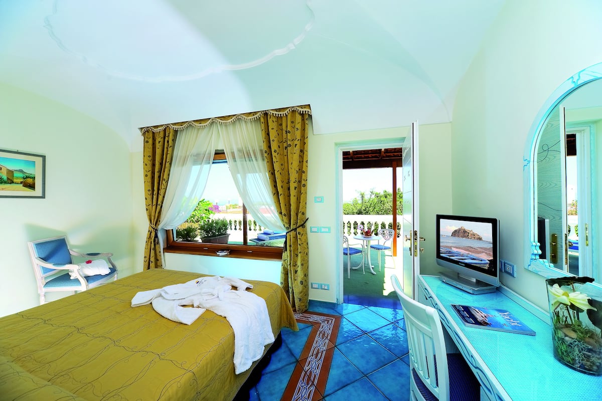 A hotel room with a bed, a desk with a computer, a TV, and a window with curtains.