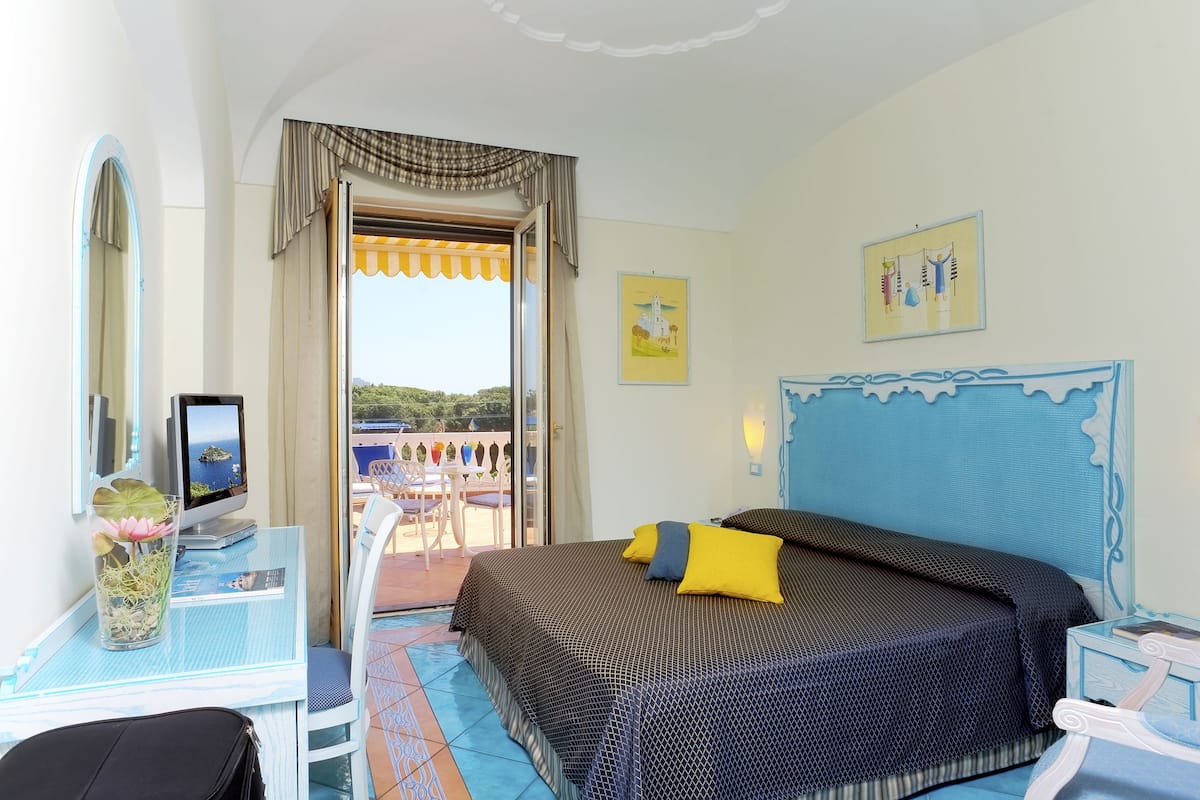 A bedroom with a bed, a desk with a computer, a chair, and a window with curtains.