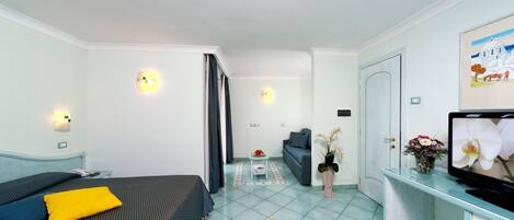 Habitación de hotel con cama, escritorio con televisor, pequeña mesa con un florero y sofá.
