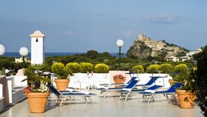 A rooftop terrace with lounge chairs, potted plants, and a view of a historic castle. - Hotel Bellevue Benessere & Relax (Ischia)