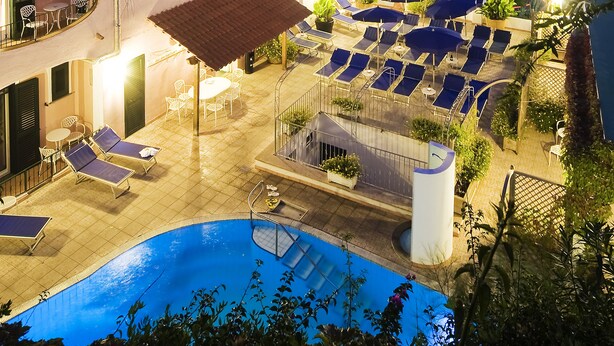 A hotel with a swimming pool, lounge chairs, and a view of the surrounding landscape. - Hotel Bellevue Benessere & Relax (Ischia)