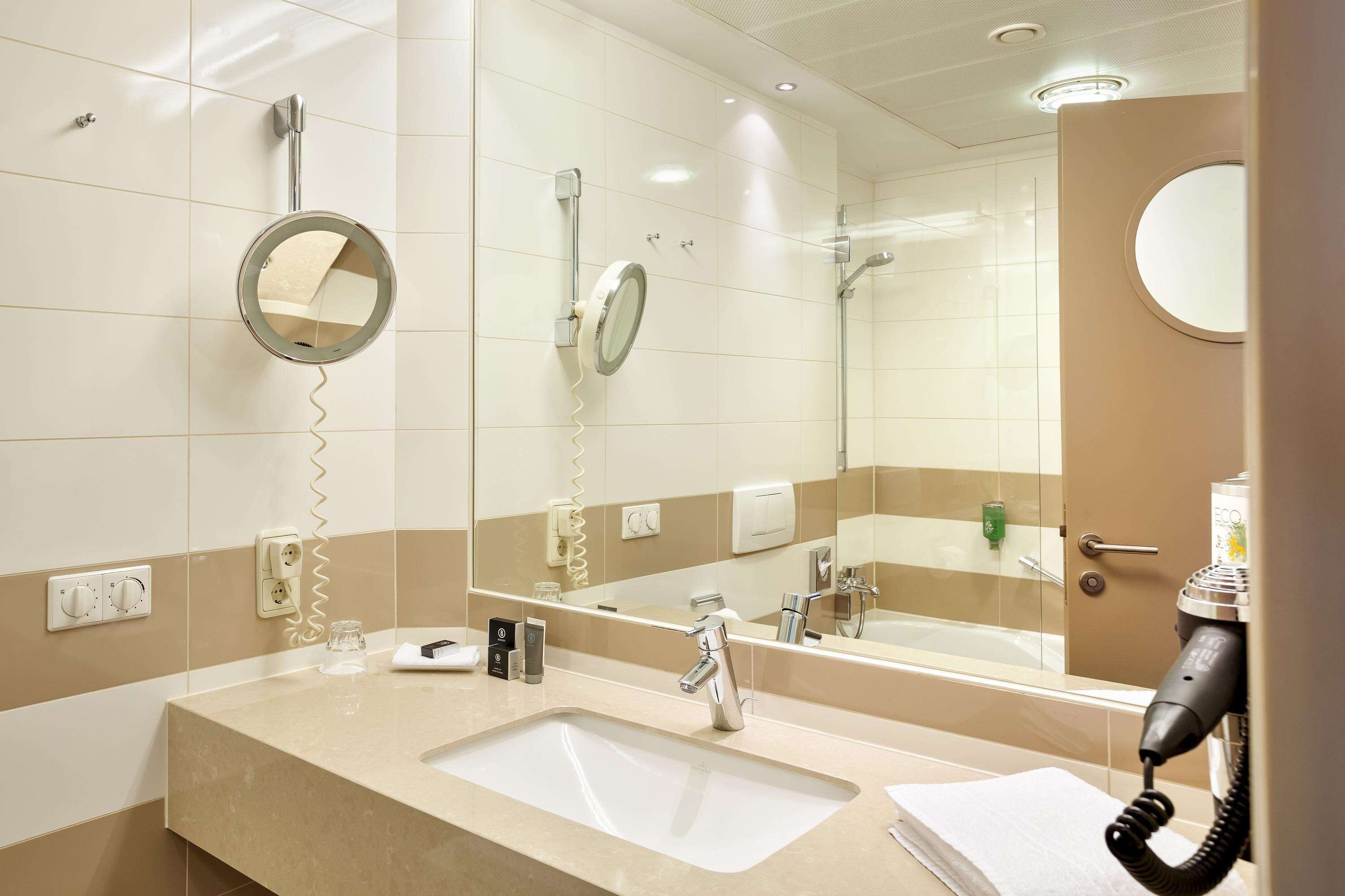 Baño de hotel con lavamanos, espejo y secador de pelo en la pared.