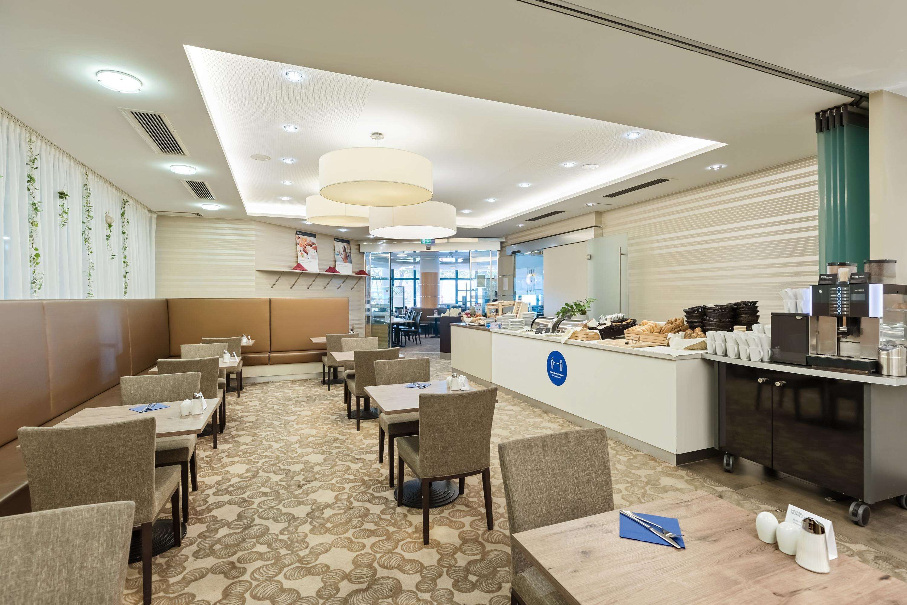 A hotel dining area with tables, chairs, a reception desk, and a kitchen area.