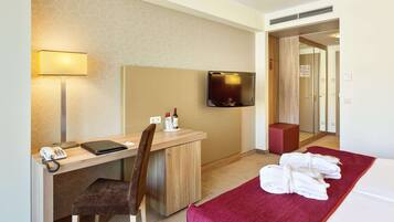 Ein Hotelzimmer mit Schreibtisch, Stuhl, Fernseher und einem Bett mit Handtüchern.