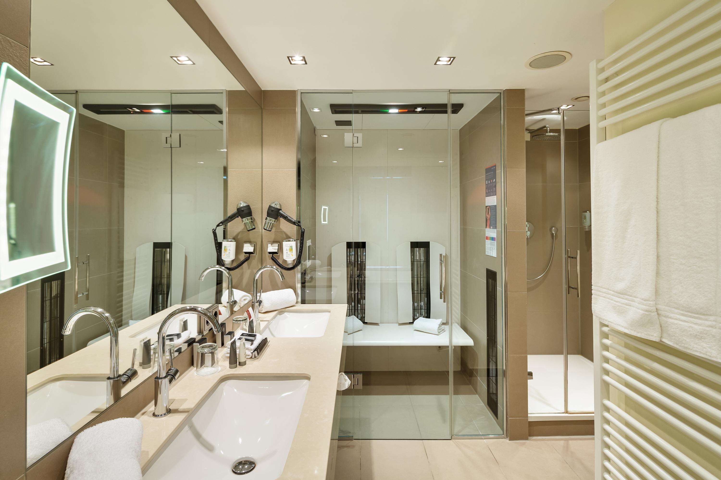 A modern bathroom with a large mirror, dual sinks, a glass-enclosed shower, and a towel rack.