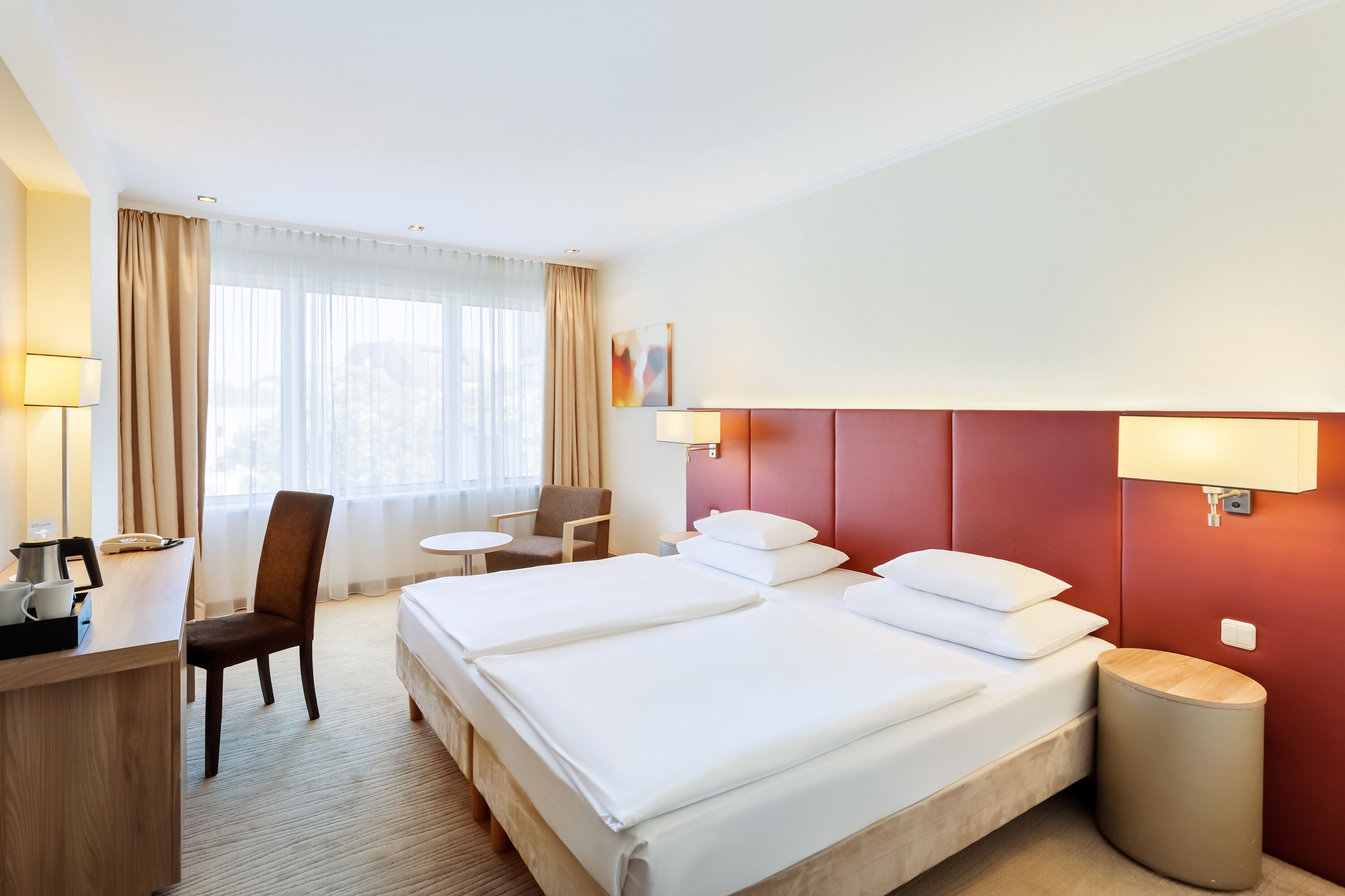 A hotel room with a bed, a desk, a chair, a lamp, and a bedside table.