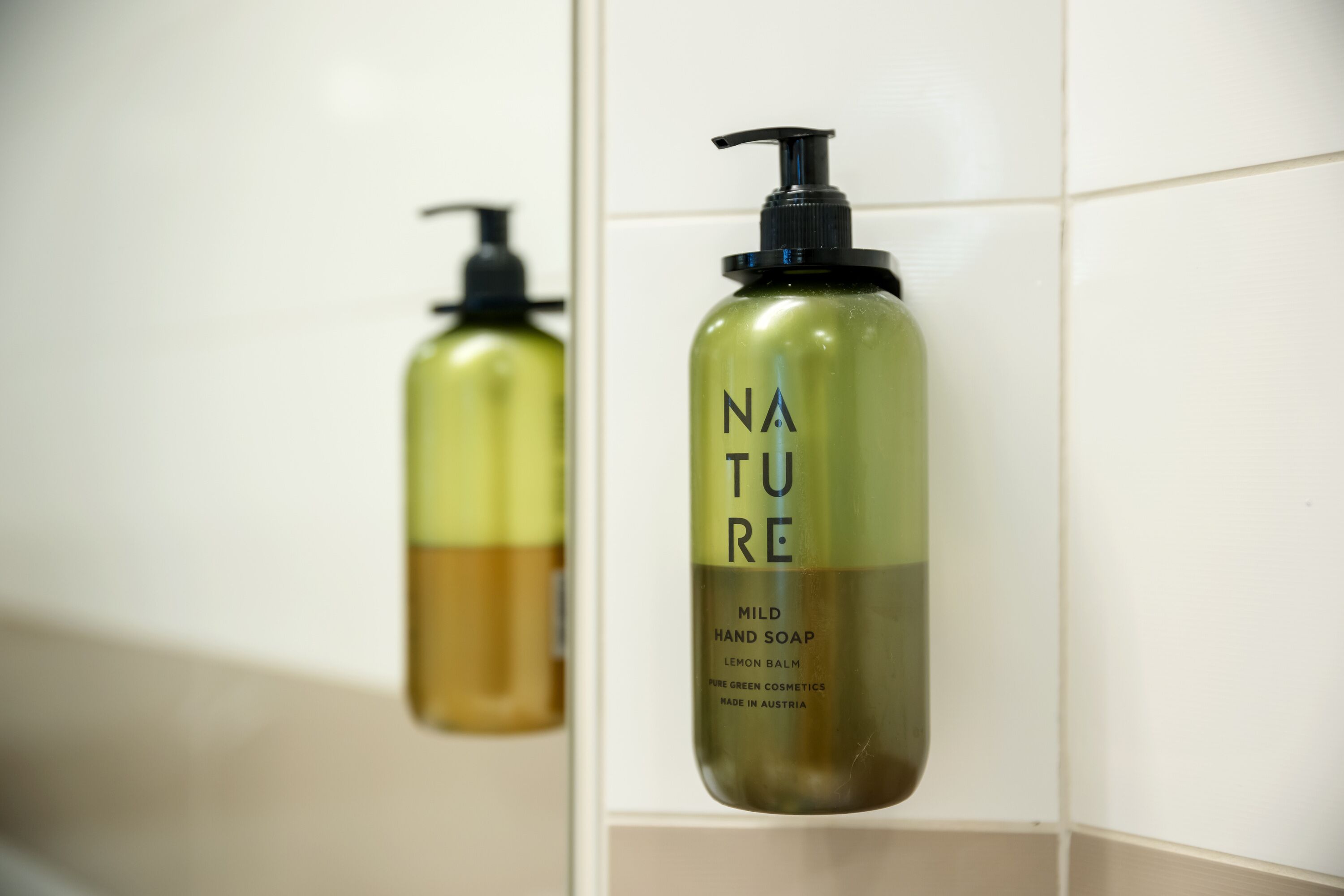 Een badkamer met een zeepdispenser aan een witte betegelde muur.