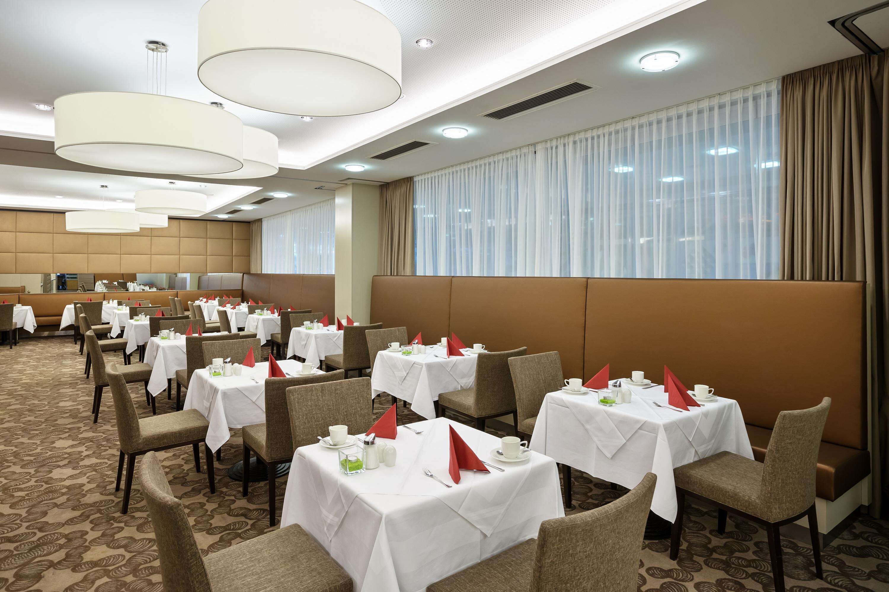 A hotel dining area with multiple tables set for dining, each with white tablecloths and red napkins.