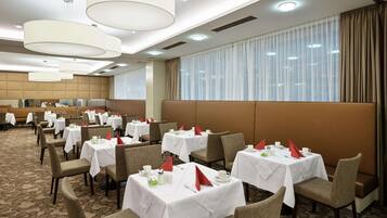 A hotel dining area with multiple tables set for dining, each with white tablecloths and red napkins.