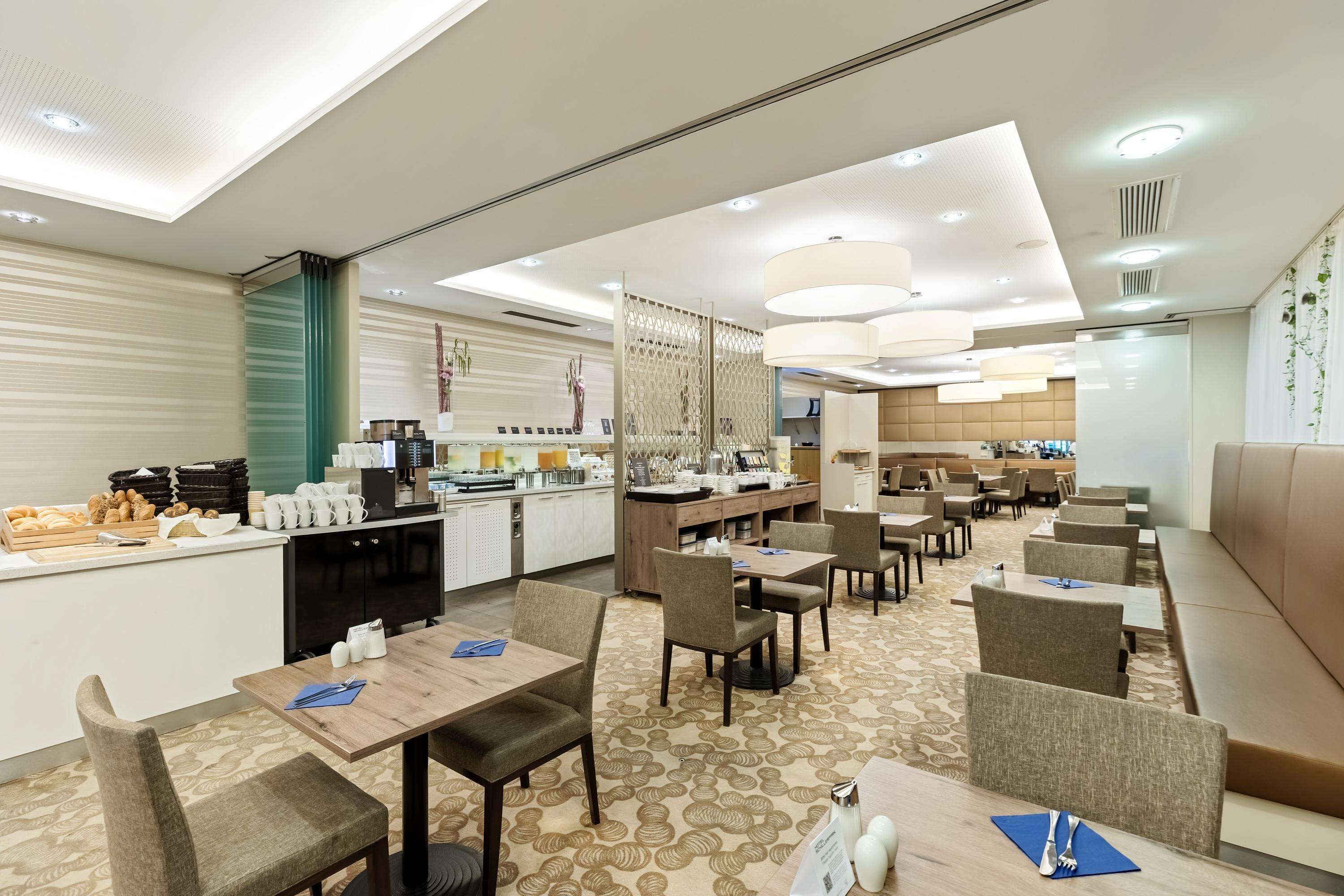 Un espace de restauration moderne dans un hôtel, avec des tables, des chaises et une cuisine en arrière-plan.