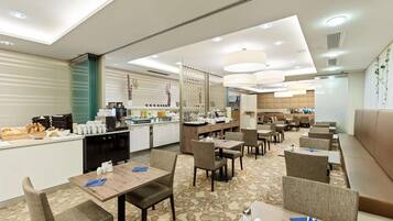 Un espace de restauration moderne dans un hôtel, avec des tables, des chaises et une cuisine en arrière-plan.