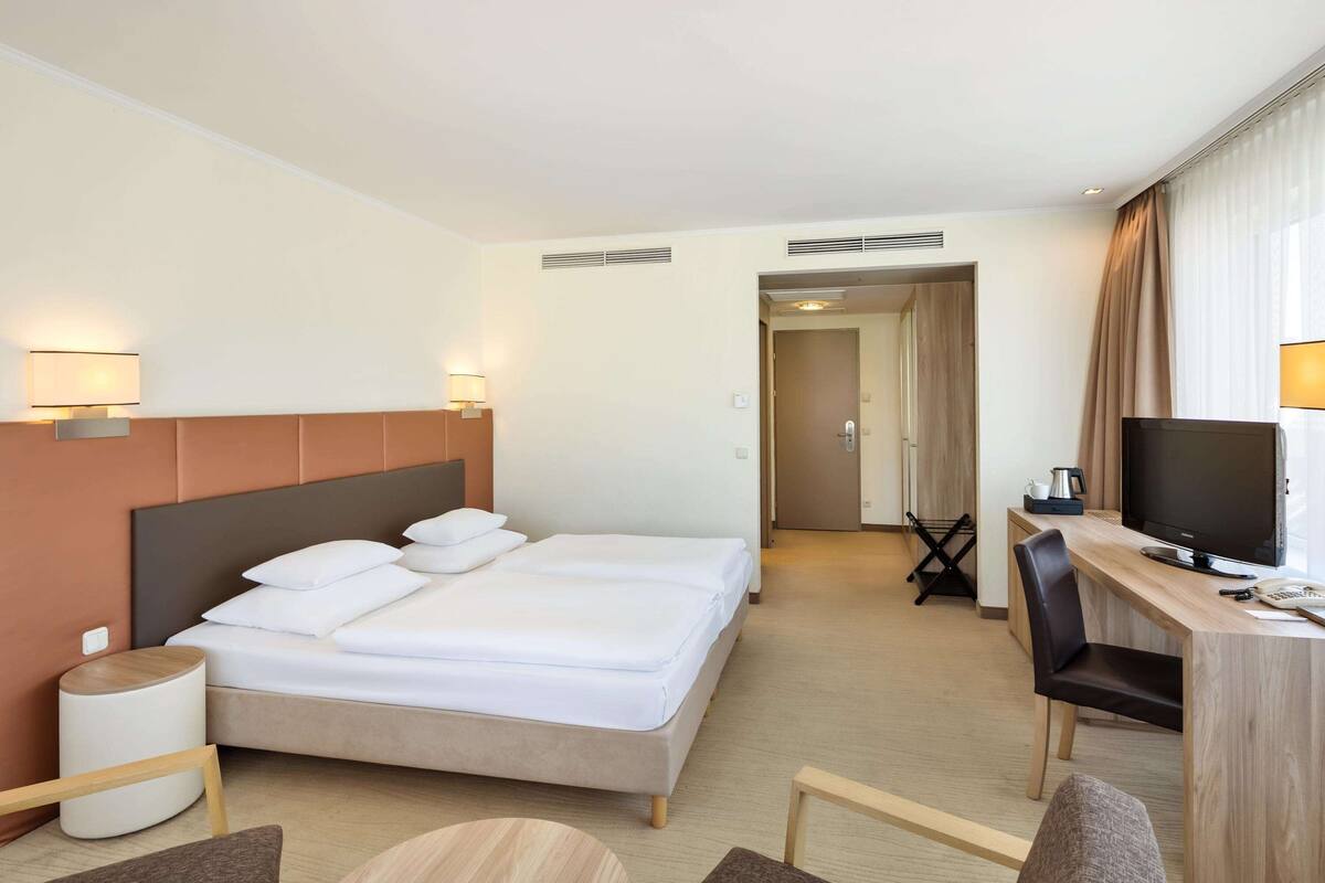 A hotel room with a double bed, a desk with a chair, a television, and a bedside table.