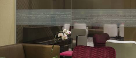 Un hall d’hôtel moderne avec un piano, un espace salon et une cloison en verre ornée d’une orchidée.