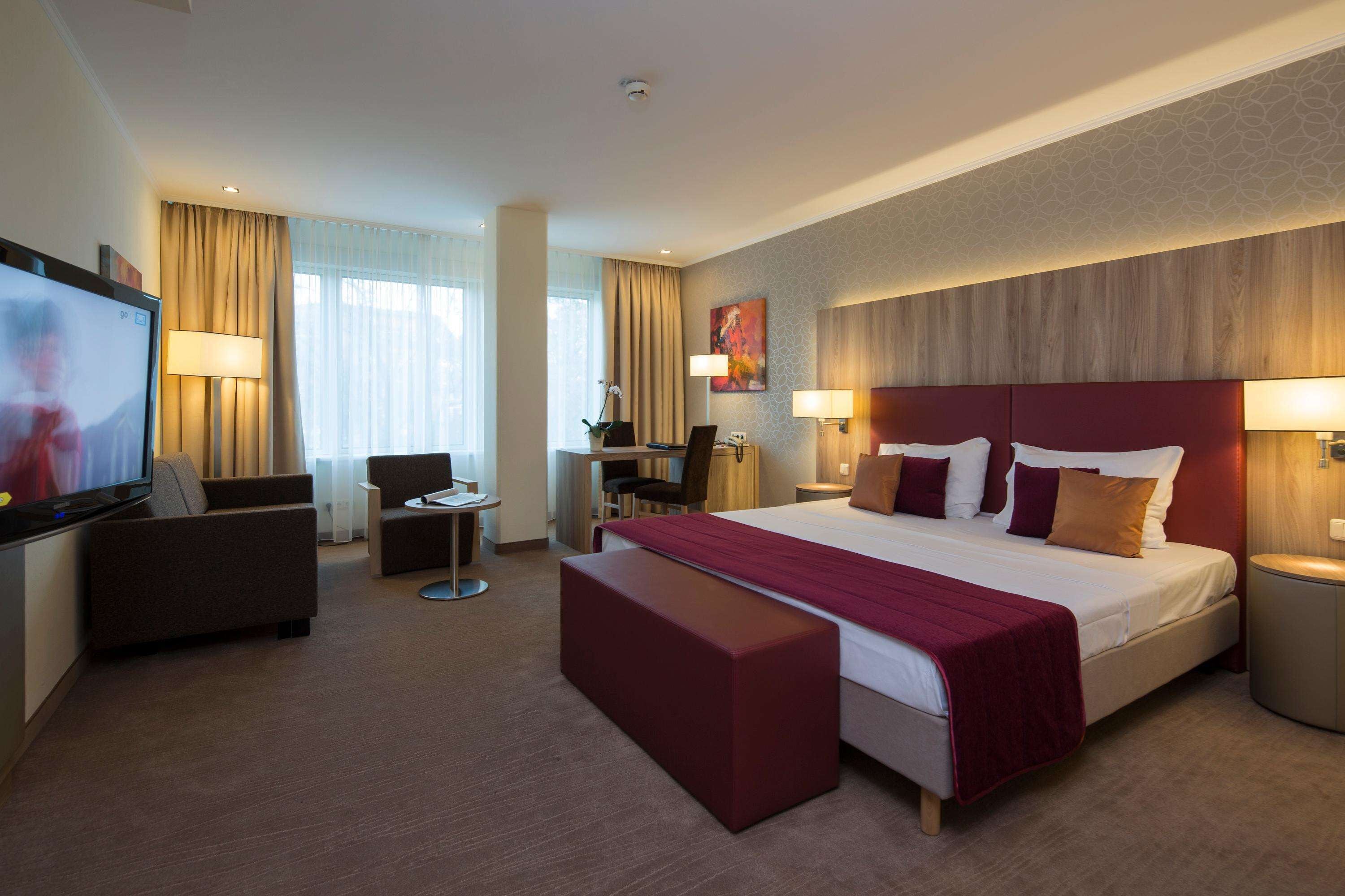 A hotel room with a large bed, a desk, a television, and a seating area.