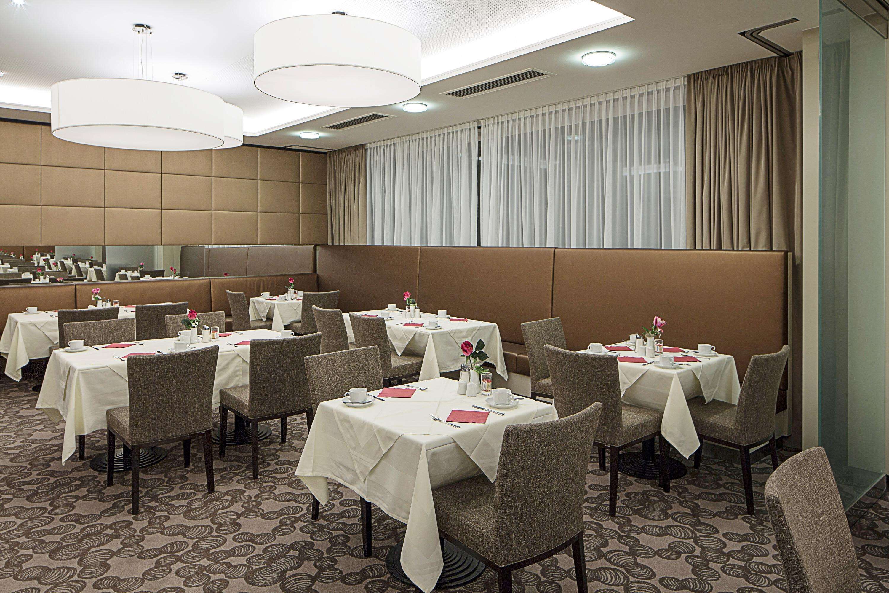 Uma sala de jantar de hotel com várias mesas, cadeiras e um espelho grande na parede.