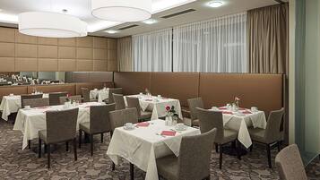 Uma sala de jantar de hotel com várias mesas, cadeiras e um espelho grande na parede.