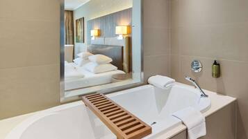 Un baño moderno con una bañera grande, un estante de madera, un perchero y un espejo que refleja la habitación.