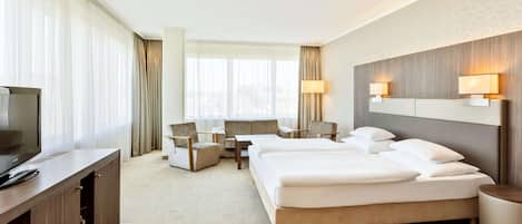 A hotel room with a bed, two armchairs, a desk, a TV, and a lamp.
