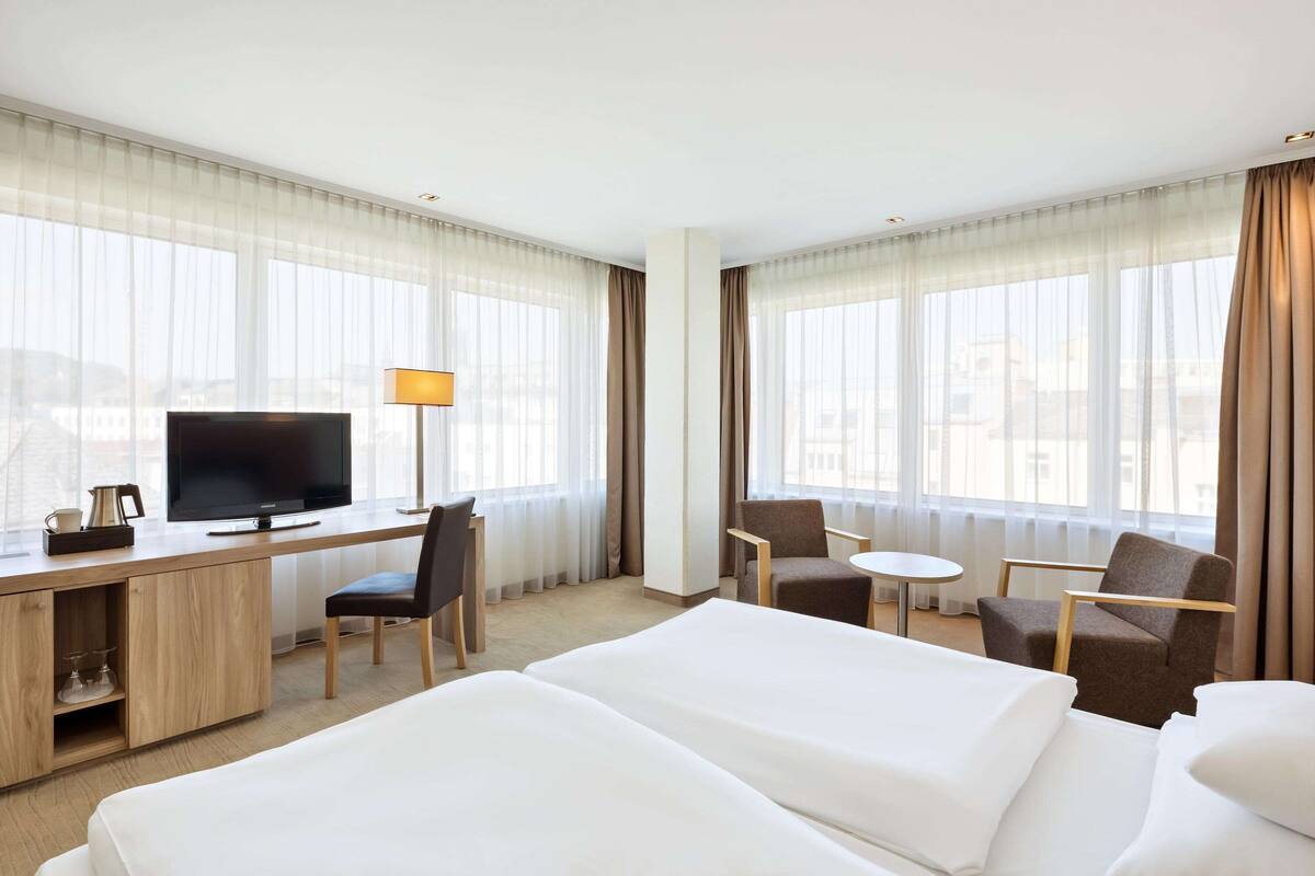 A hotel room with a bed, a desk with a TV, two chairs, and a small table.