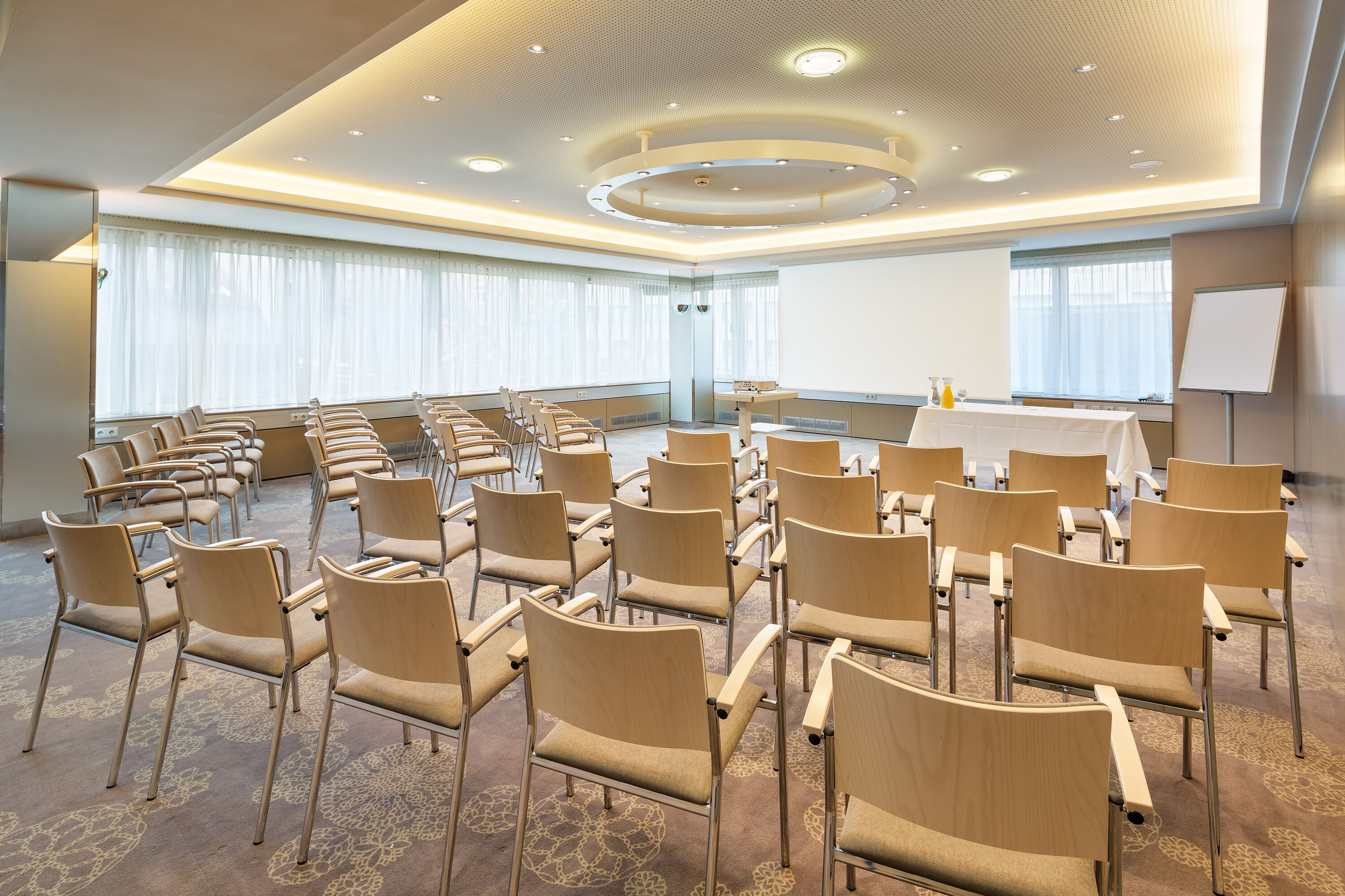 Un salón de conferencias con filas de sillas, una pantalla de proyector y una pizarra.