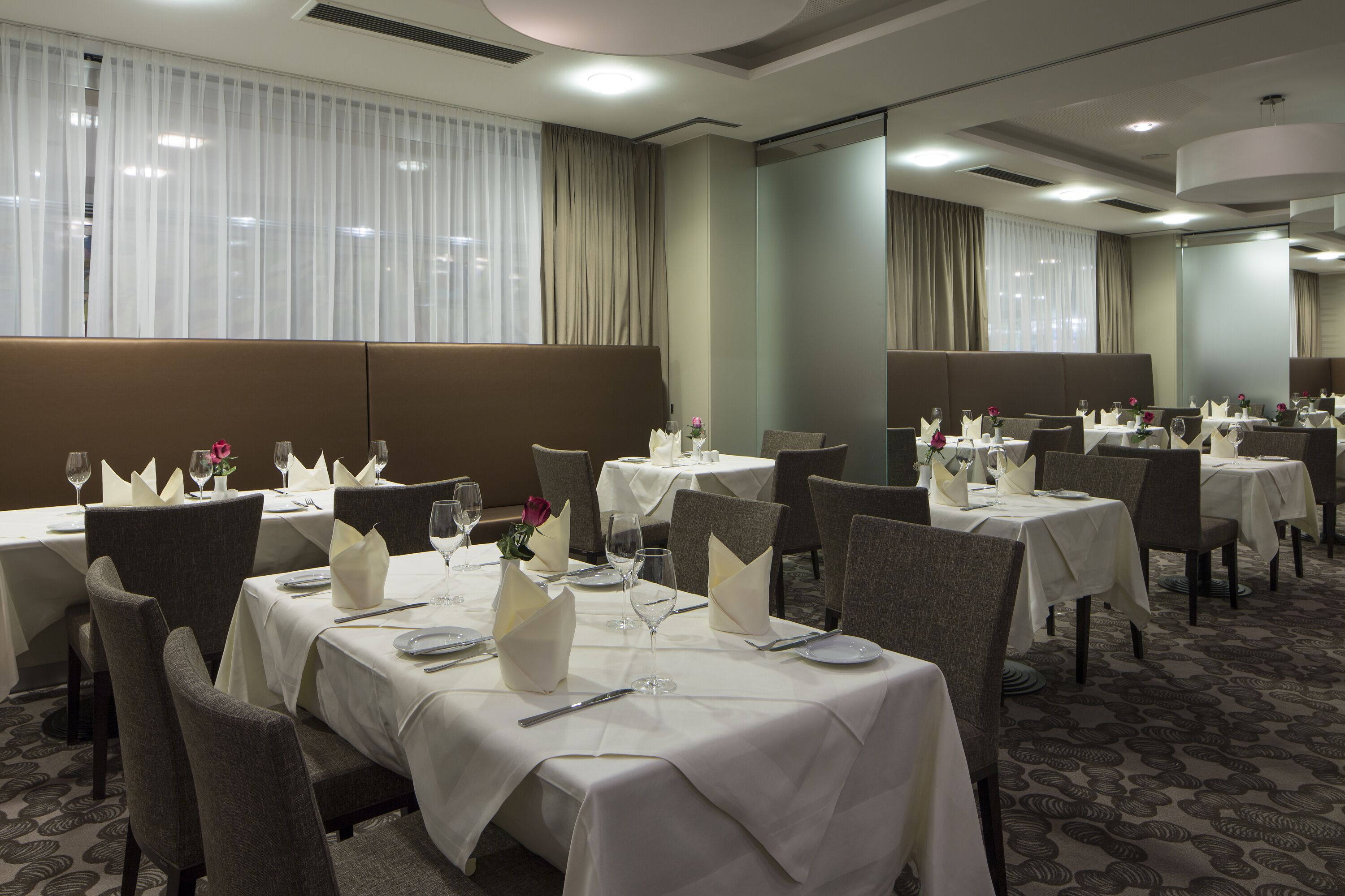 A hotel dining area with multiple tables set for dining, each with white tablecloths and silverware.