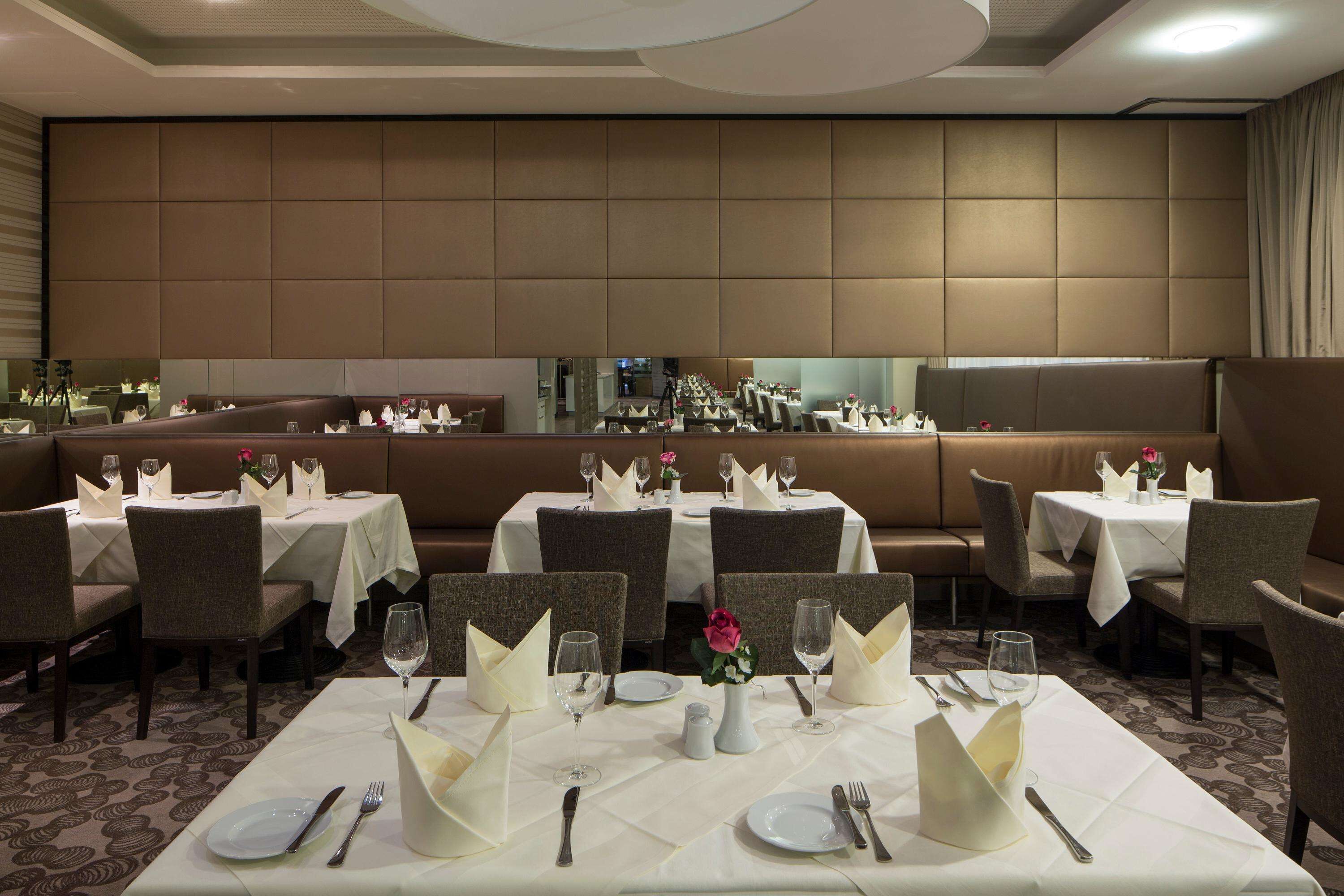 A restaurant with multiple tables set for dining, featuring white tablecloths, neatly arranged cutlery, and a vase with flowers.