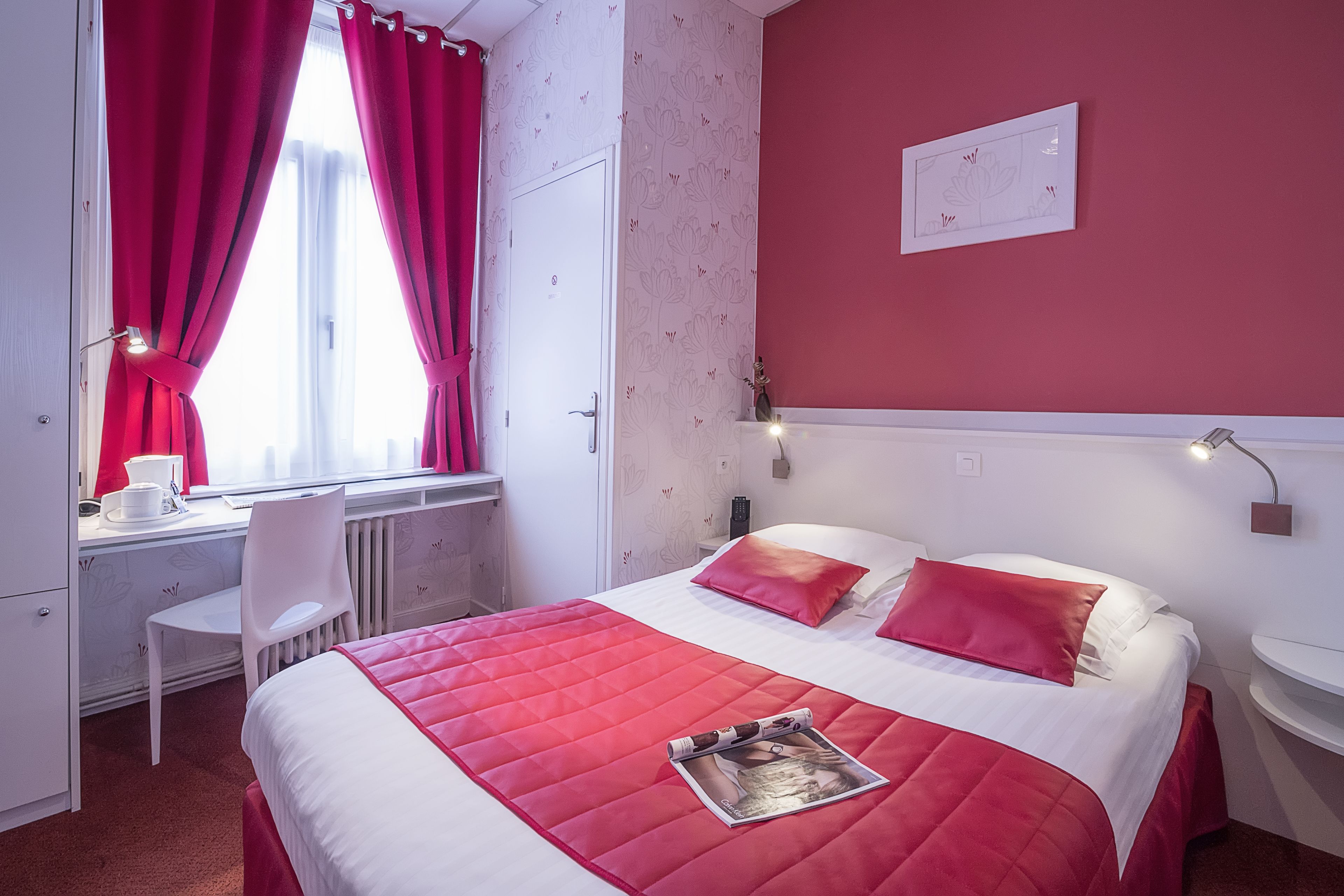Une chambre d’hôtel avec un lit, un bureau, une chaise et une fenêtre avec des rideaux.