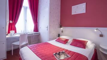 Une chambre d’hôtel avec un lit, un bureau, une chaise et une fenêtre avec des rideaux.
