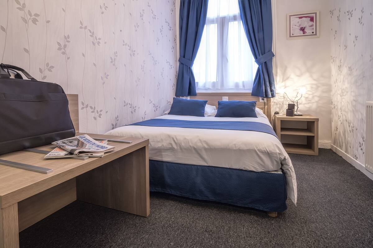 Ein Hotelzimmer mit Bett, Schreibtisch, Stuhl und einem fenster mit Vorhängen.