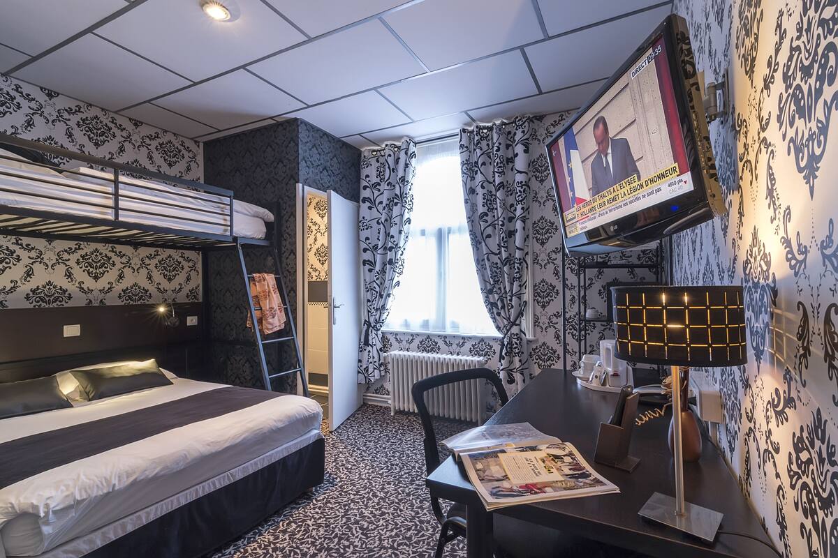 Ein Hotelzimmer mit Etagenbett, Schreibtisch mit Lampe, Fernseher und Wandpapier mit Muster.