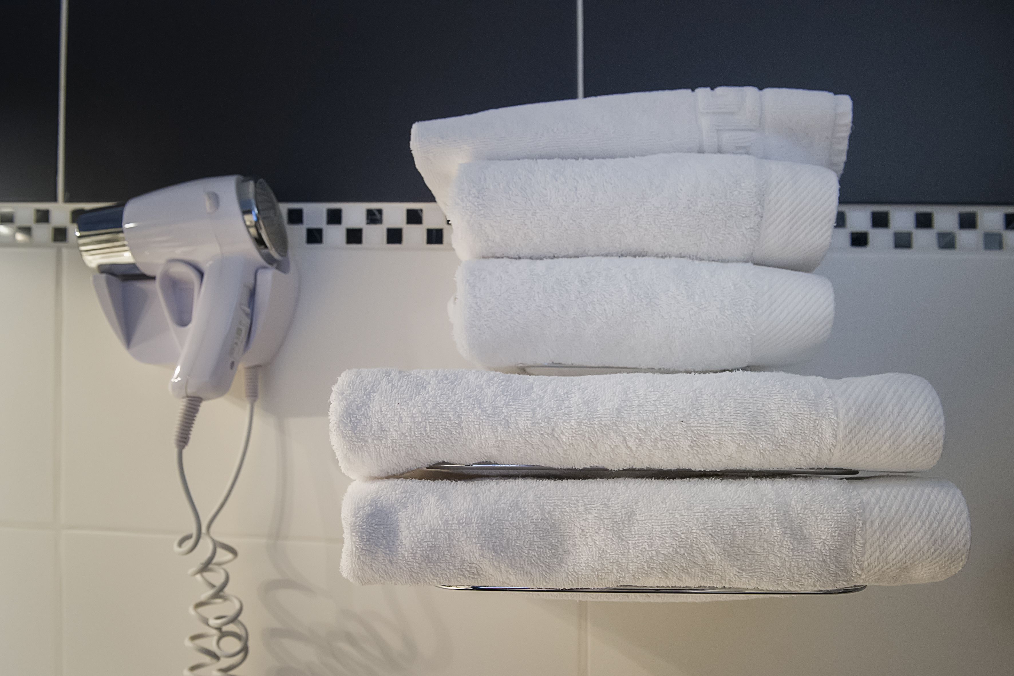 A wall-mounted hairdryer and neatly stacked towels.