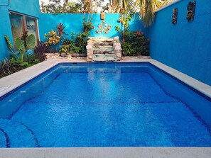 Una piscina rectangular con agua azul cristalina, rodeada por un muro azul con detalles decorativos y plantas.