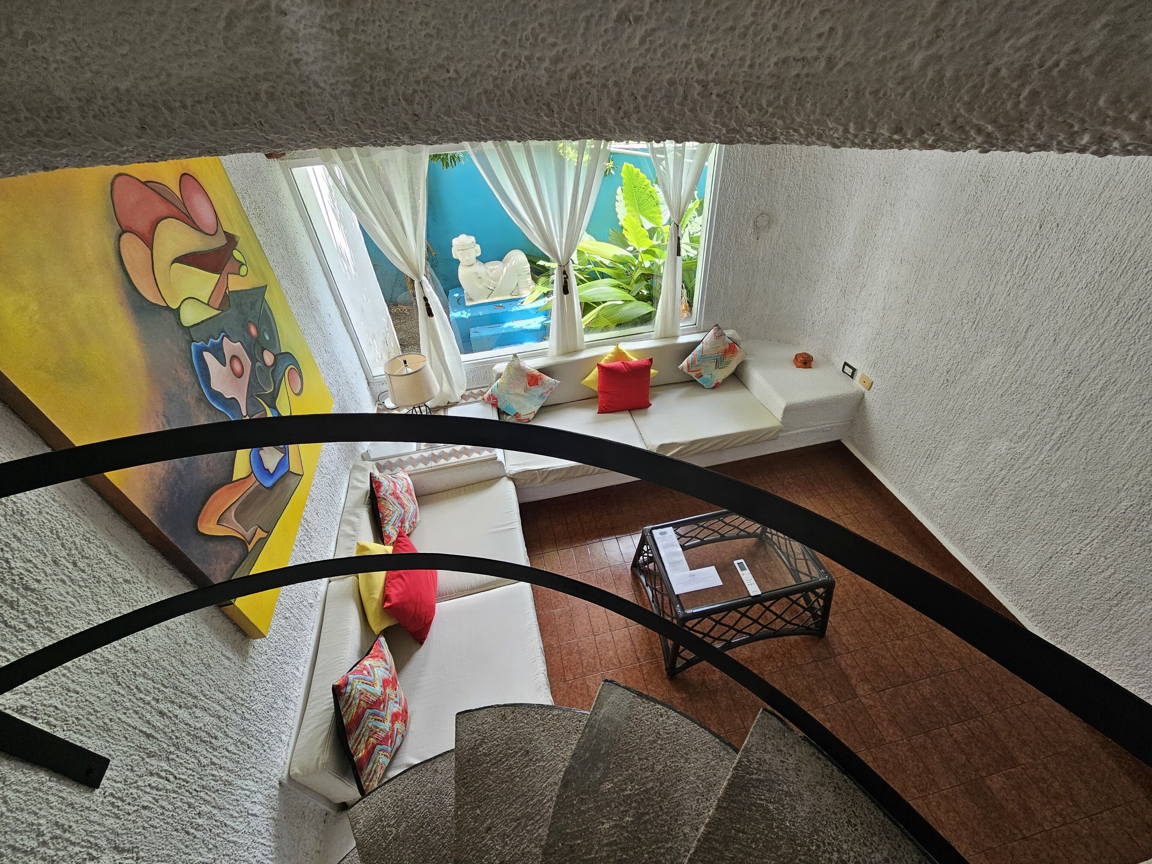 Una habitación con ventana, un sofá, una mesita y una escalera.