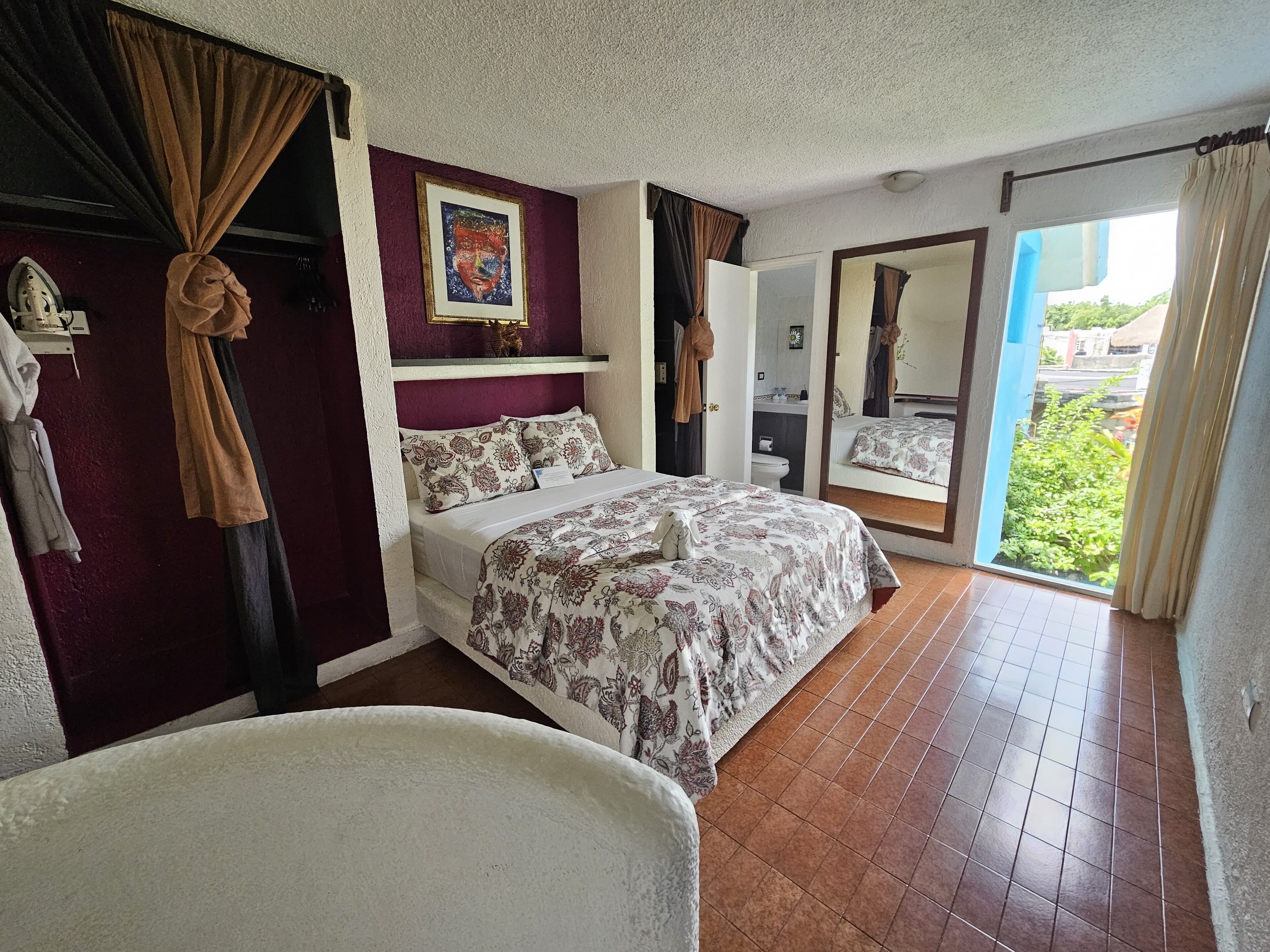 A hotel room with a bed, a chair, a bathroom, and a balcony with curtains.