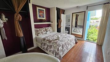 A hotel room with a bed, a chair, a bathroom, and a balcony with curtains.