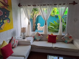 A room with a white sofa, colorful cushions, a lamp, and a view of greenery and a statue outside.