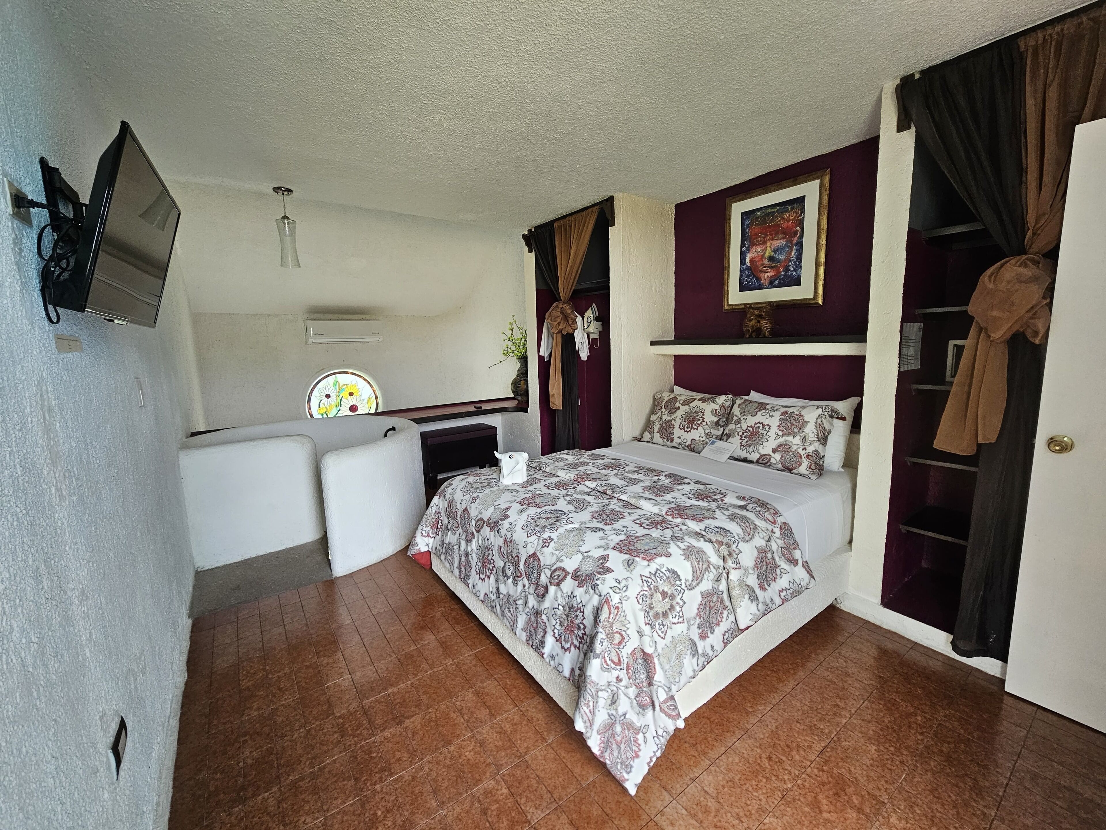 Quarto com uma cama, escrivaninha, televisão e guarda-roupa.